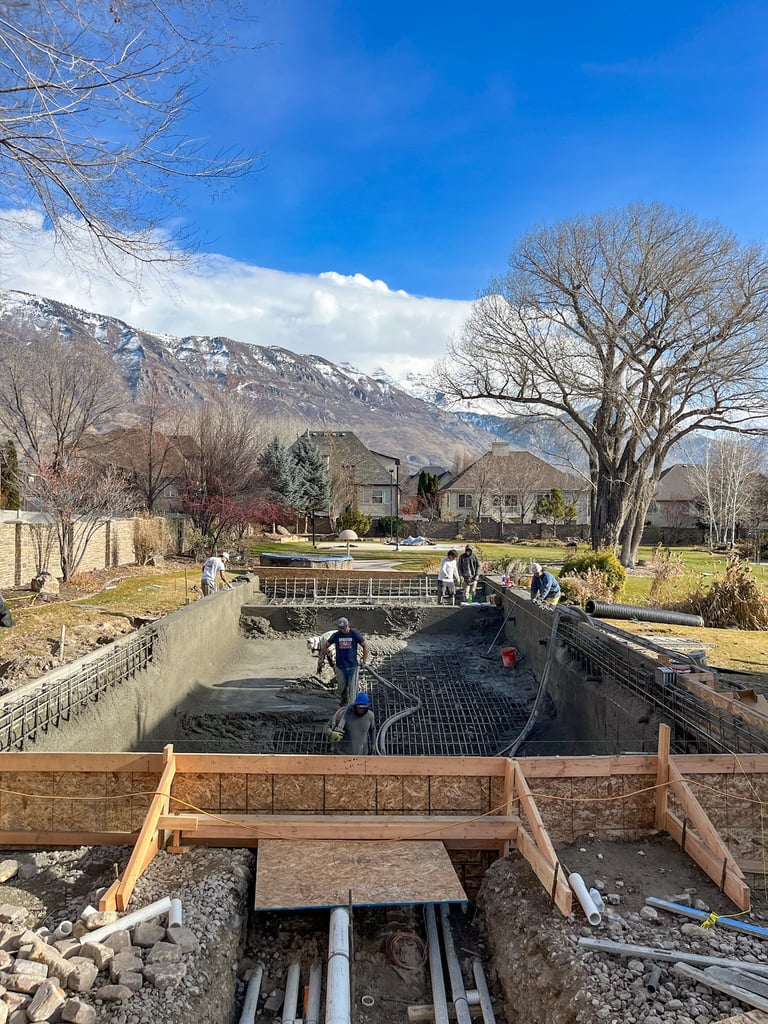 Construction site with underground excavation, wooden forms, and snow-capped mountains in background under blue sky