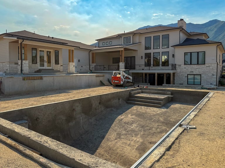 Modern residential home under construction with an empty concrete pool foundation and mountain views in background