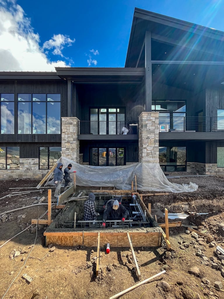Construction workers under tarping at the base of a modern multi-story building with stone columns and large windows