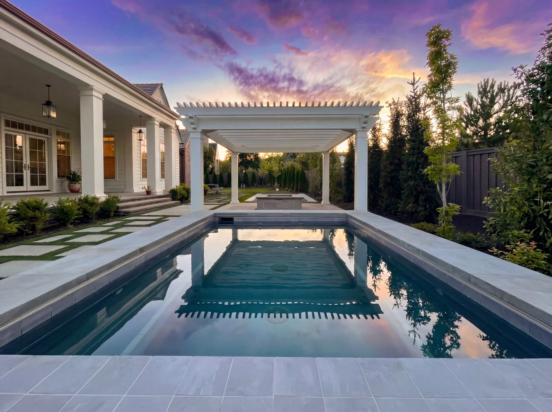 Modern house with covered patio, rectangular pool, and manicured landscaping during sunset