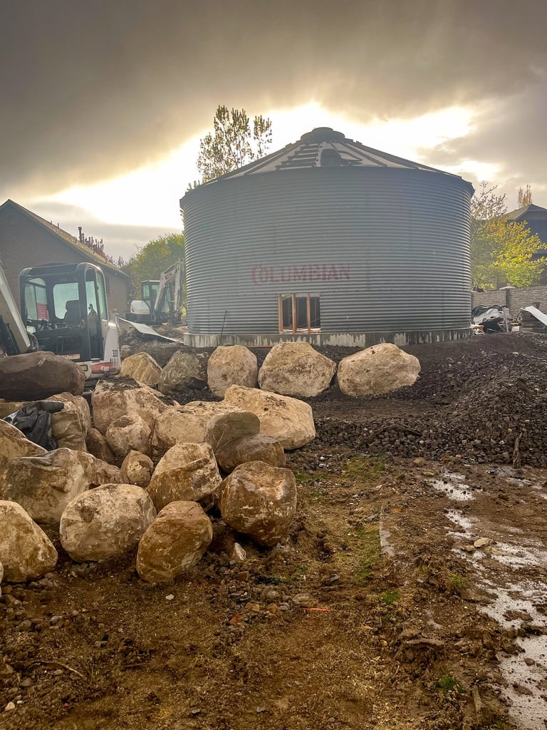 Large metal grain silo on farm with pile of boulders in foreground and cloudy sky overhead