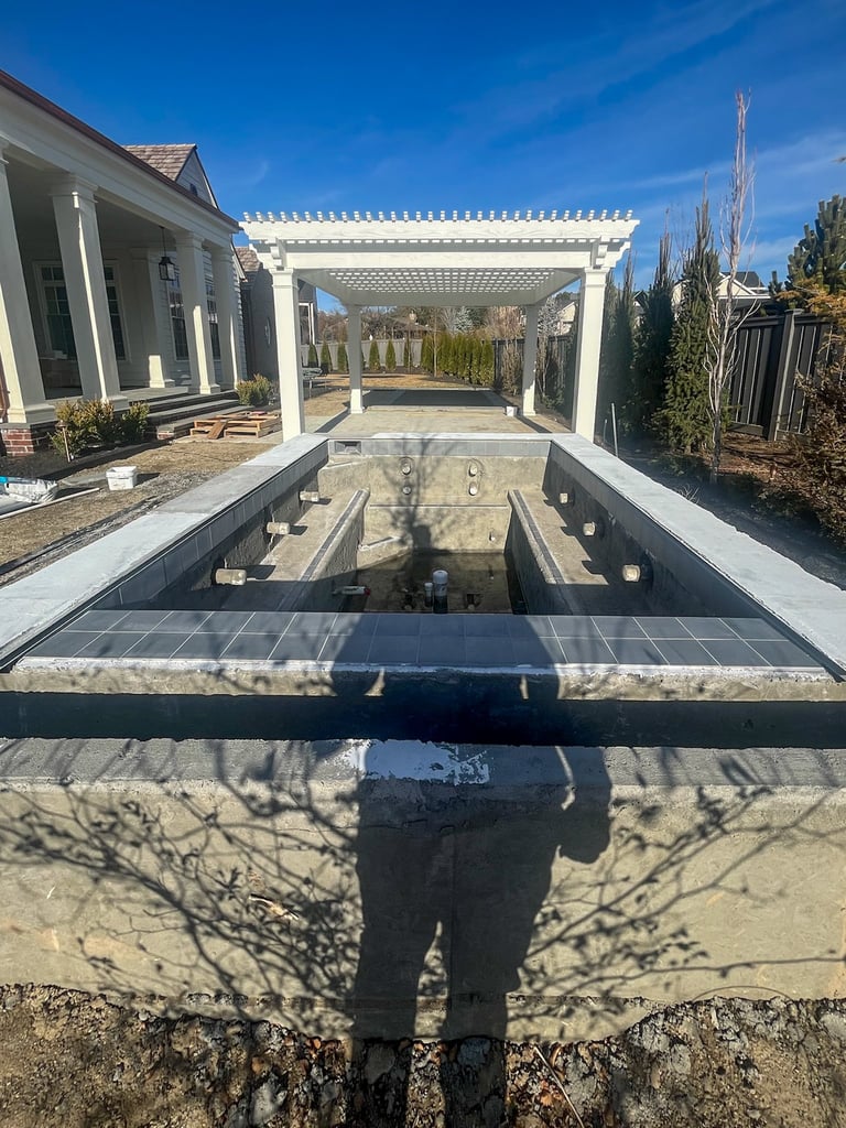 White pergola structure attached to modern home with pool channel, cypress trees visible, blue sky overhead