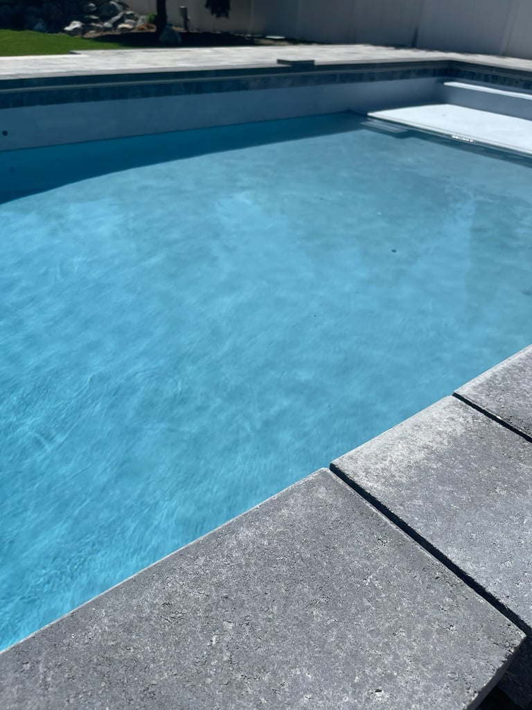 Empty residential swimming pool with clear blue water, concrete deck, and white diving board