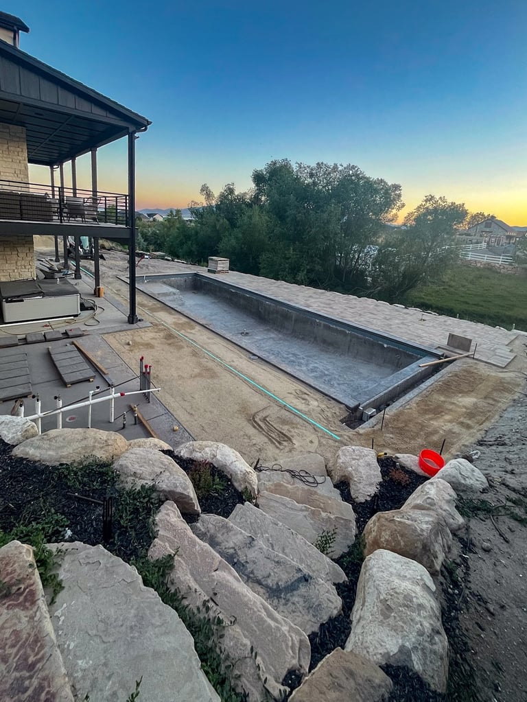 Modern hillside home with elevated deck overlooking an empty rectangular pool under construction at sunset