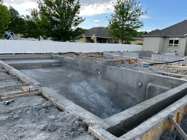 In-ground concrete pool under construction with wooden framing in residential backyard setting