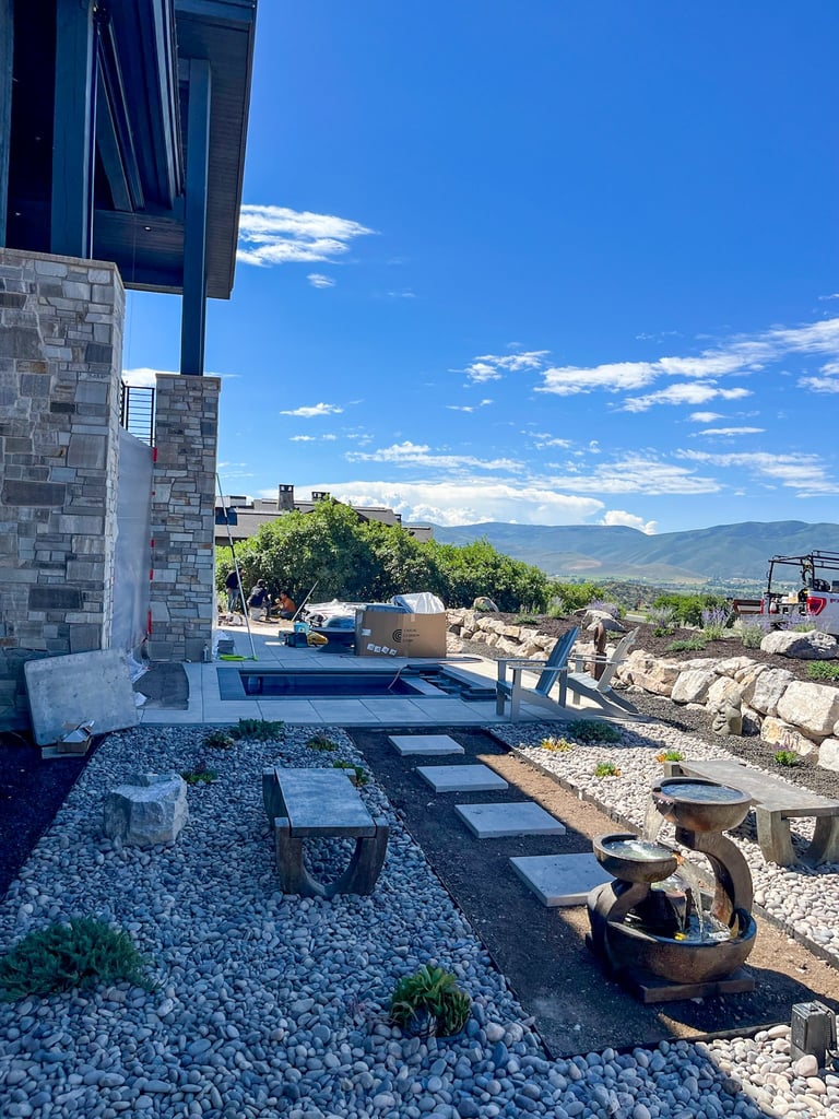 Modern hillside home with stone patio, gravel courtyard, and mountain valley views under blue sky with clouds