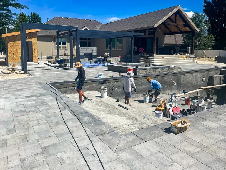 Workers constructing a large paved patio area next to a modern home with mountains in the background