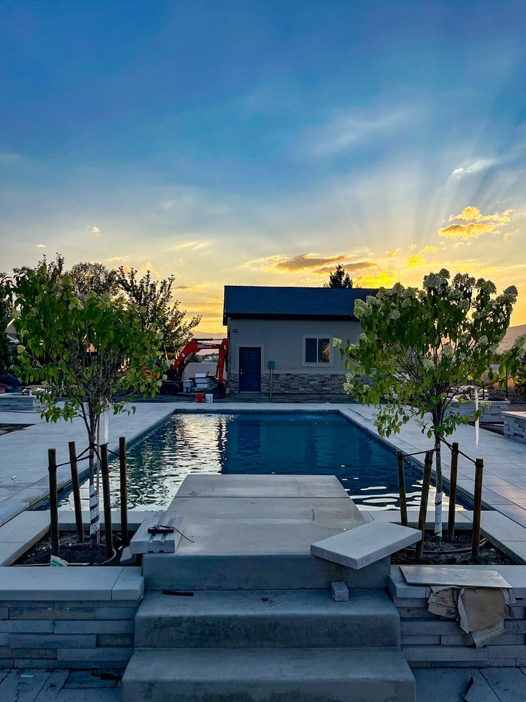 Modern pool house with rectangular swimming pool at sunset, surrounded by potted trees and stone patio decking