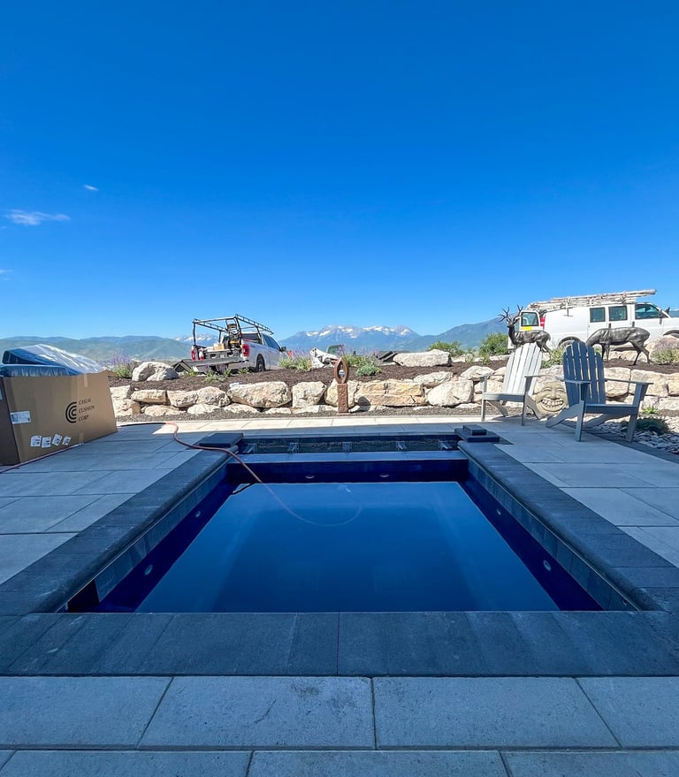 Modern rectangular swimming pool with deep blue water on a stone patio, surrounded by desert landscape and mountains in the background