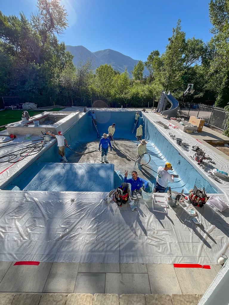 Empty swimming pool being drained and prepared for renovation with workers and equipment, mountains visible in background
