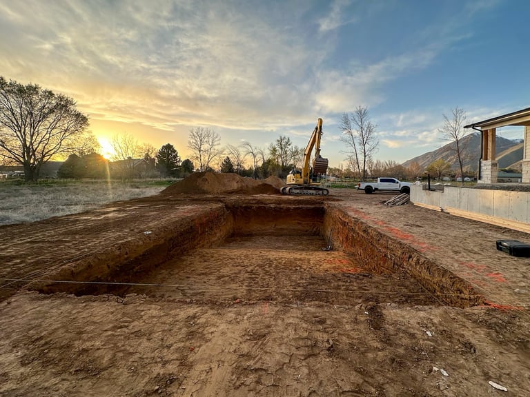 Large excavation pit at sunset with construction equipment and machinery on a cleared site surrounded by bare trees