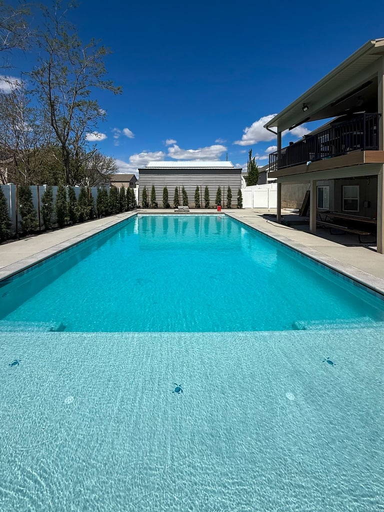 Modern luxury home with a long rectangular turquoise swimming pool, concrete deck, and contemporary architecture against a clear blue sky