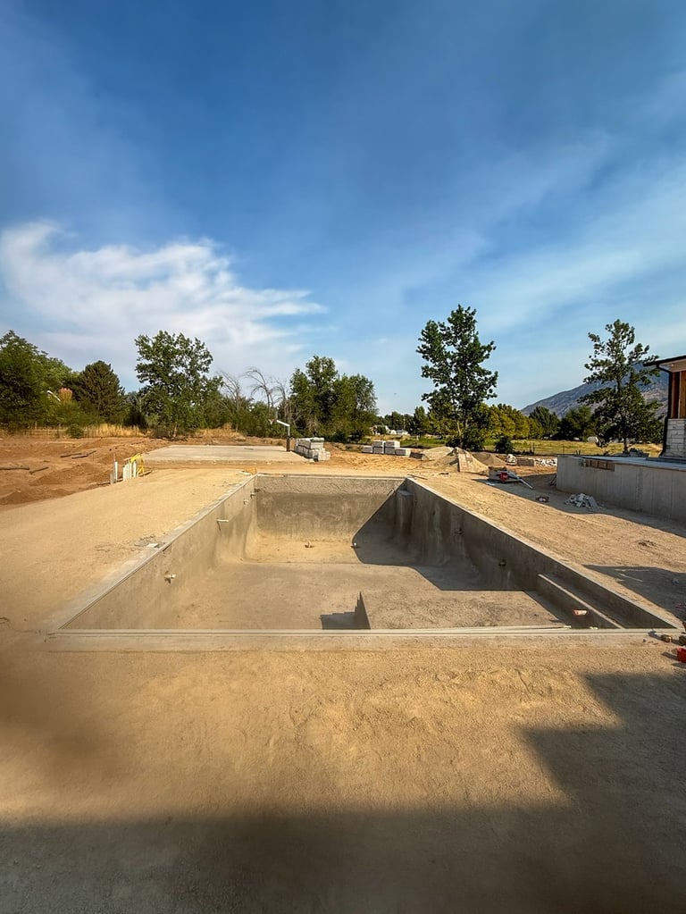 Empty concrete foundation and pool structure under construction on sandy ground with trees and blue sky