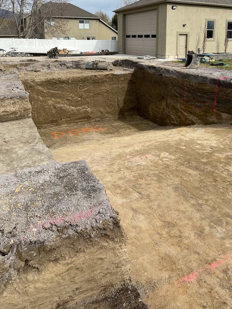 Excavated foundation pit with dirt walls in a residential backyard construction site, marked with red paint