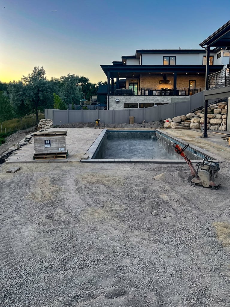 Modern two-story home with pool under construction, gravel patio, gray fence, and landscaping in evening light